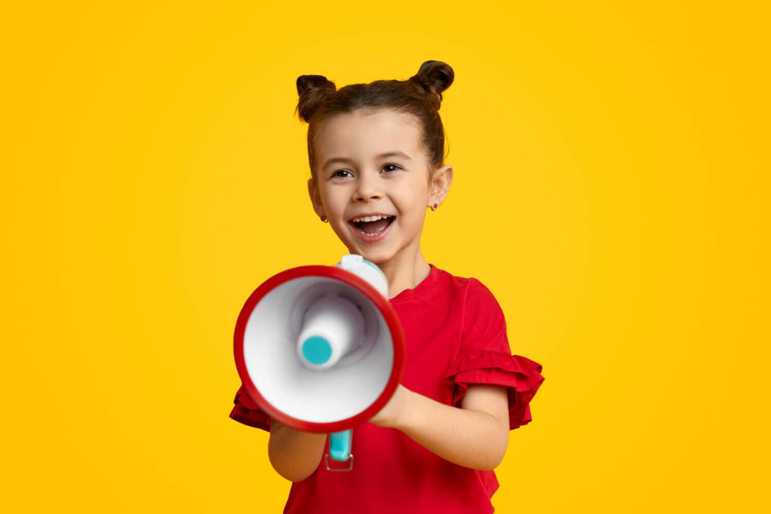 Excited kid leader speaking in megaphone and smiling while standing against yellow background. Young leader concept