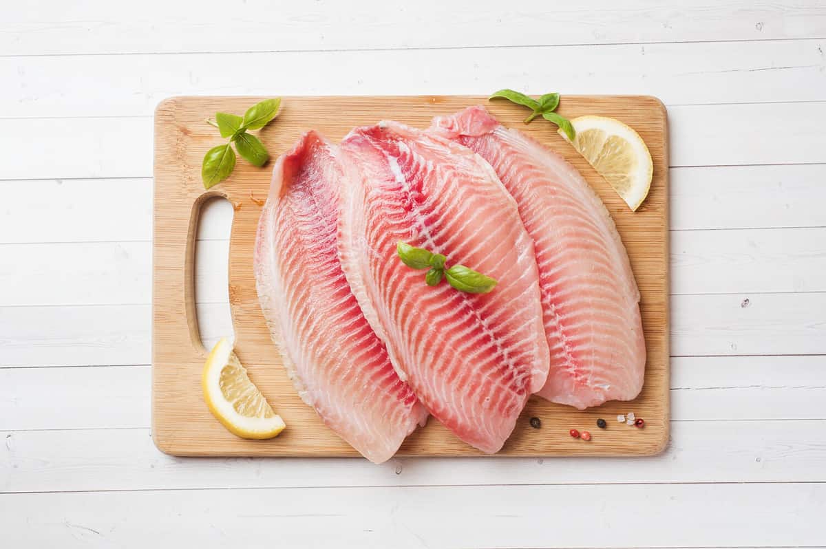 Raw fish fillet of tilapia on a cutting Board with lemon and spices. White table with copy space