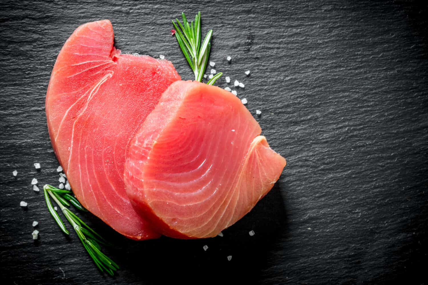 Fresh raw tuna steak with rosemary. On black rustic background