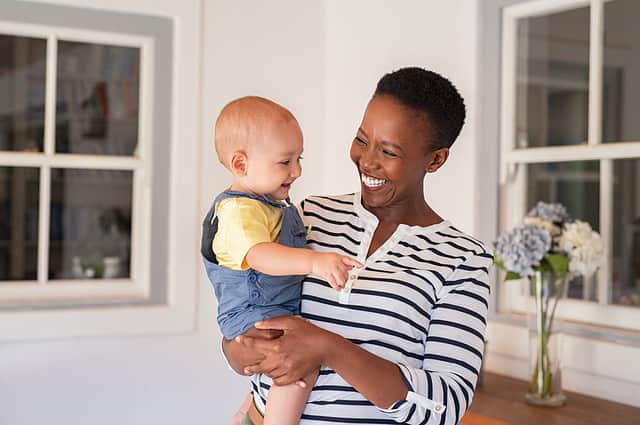 Portrait of happy black mother holding cute toddler laughing together at home. Cheerful african woman cuddling smiling little boy in hand and playing. Mature black nanny playing with little boy.