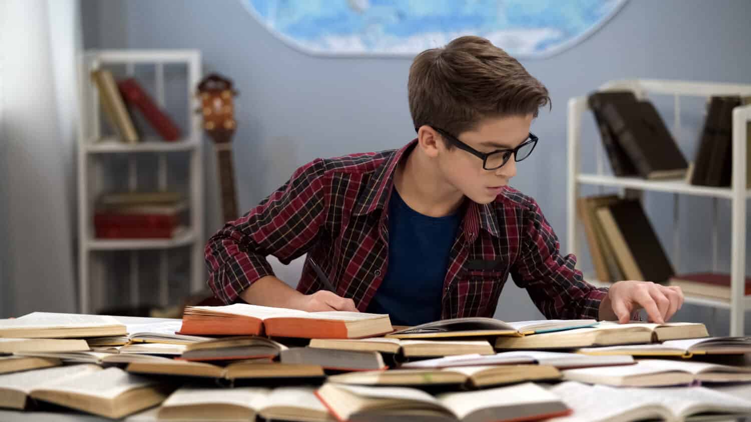 Hardworking male teen searching information sitting table full of books, student