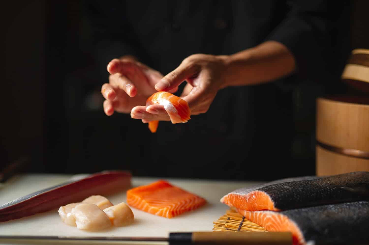 Closeup of chef hands preparing japanese food. Japanese chef making sushi at restaurant. Young chef making traditional japanese sushi on cuting board .