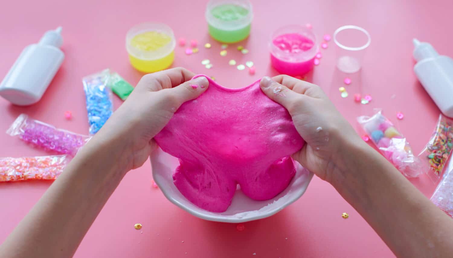 a girl making slime herself. child making slime on pink background.