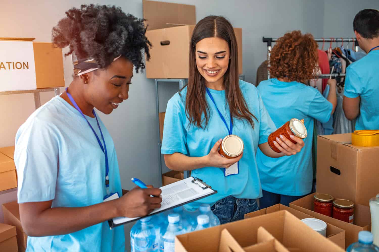 Group of people working in charitable foundation. Happy volunteer looking at donation box on a sunny day. Happy volunteer separating donations stuffs. Volunteers sort donations during food drive