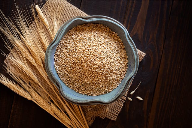 Overhead view of steel cut oats in a small bowl on a wooden surface with an accent of burlap and dried oat stems