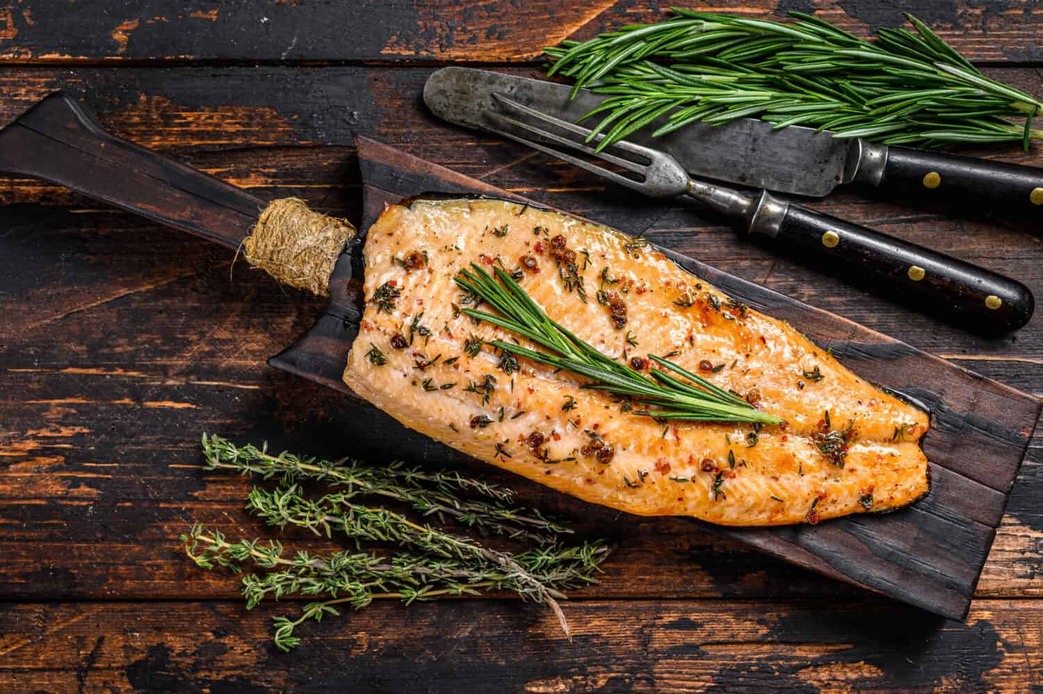 Baked trout fillet on a cutting board. Dark wooden background. Top view.