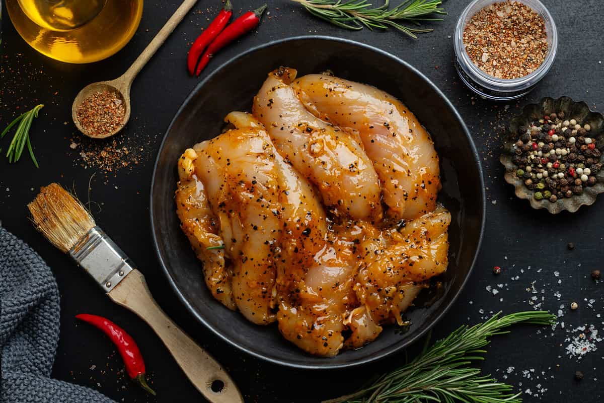 Raw marinated chicken breast on dark background with spices ready to cook.