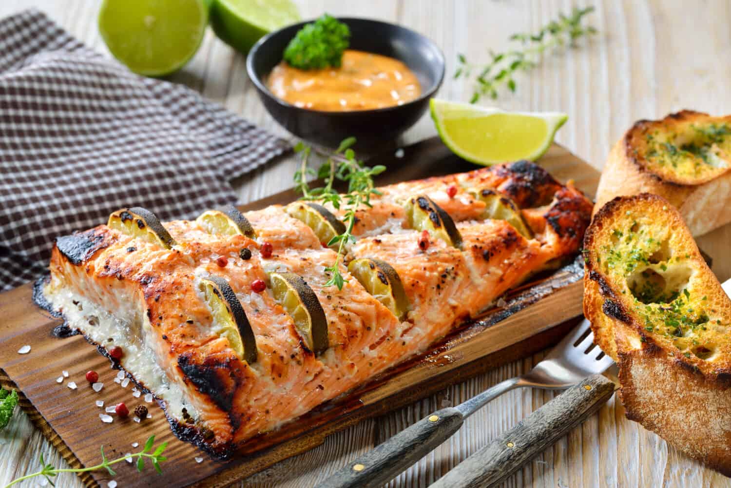 Juicy salmon fillet with lime slices on a cedar wood grilling plank fresh from the kettle grill