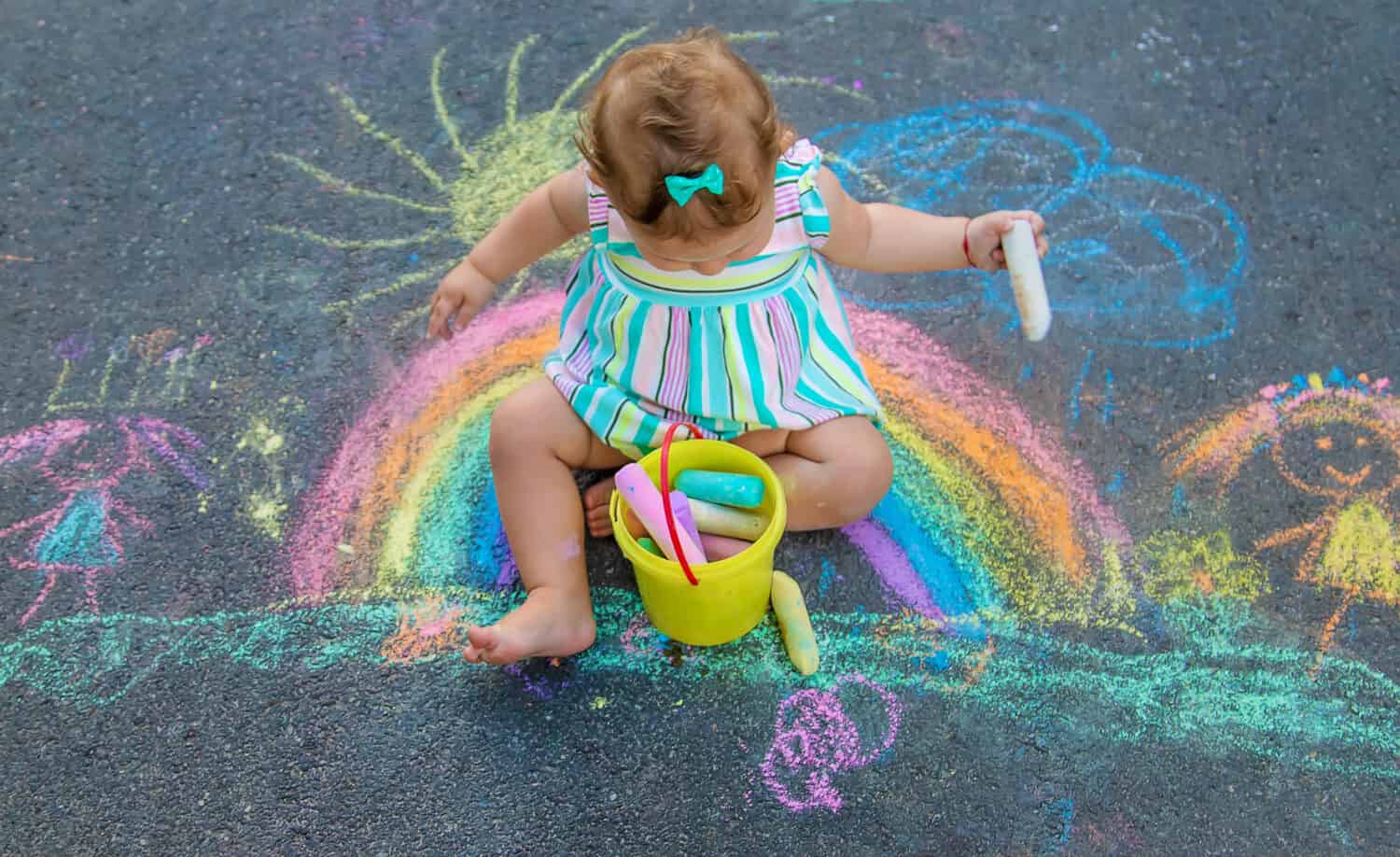 Baby draws a rainbow on the pavement with chalk. Selective focus. Nature.