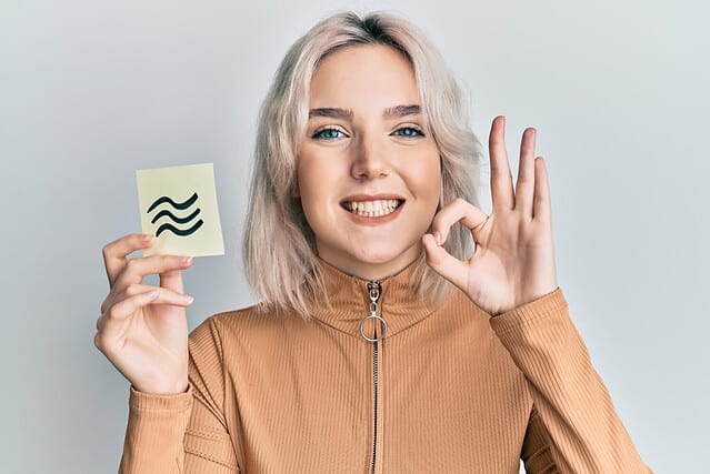 Young blonde girl holding paper with aquarius zodiac sign doing ok sign with fingers, smiling friendly gesturing excellent symbol