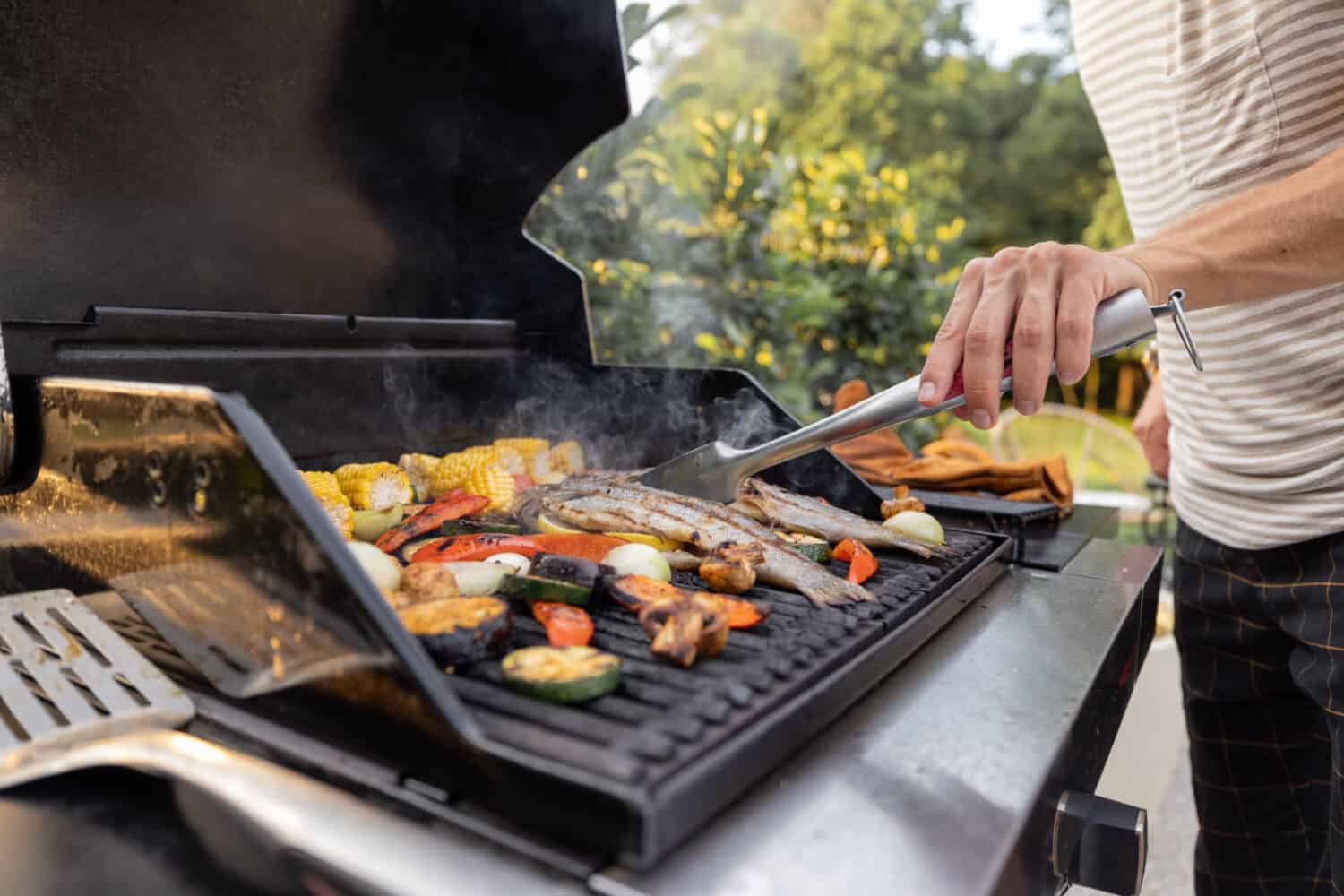 People grilling fish and corn on a modern grill outdoors at sunet, close-up. Cooking food on the open air