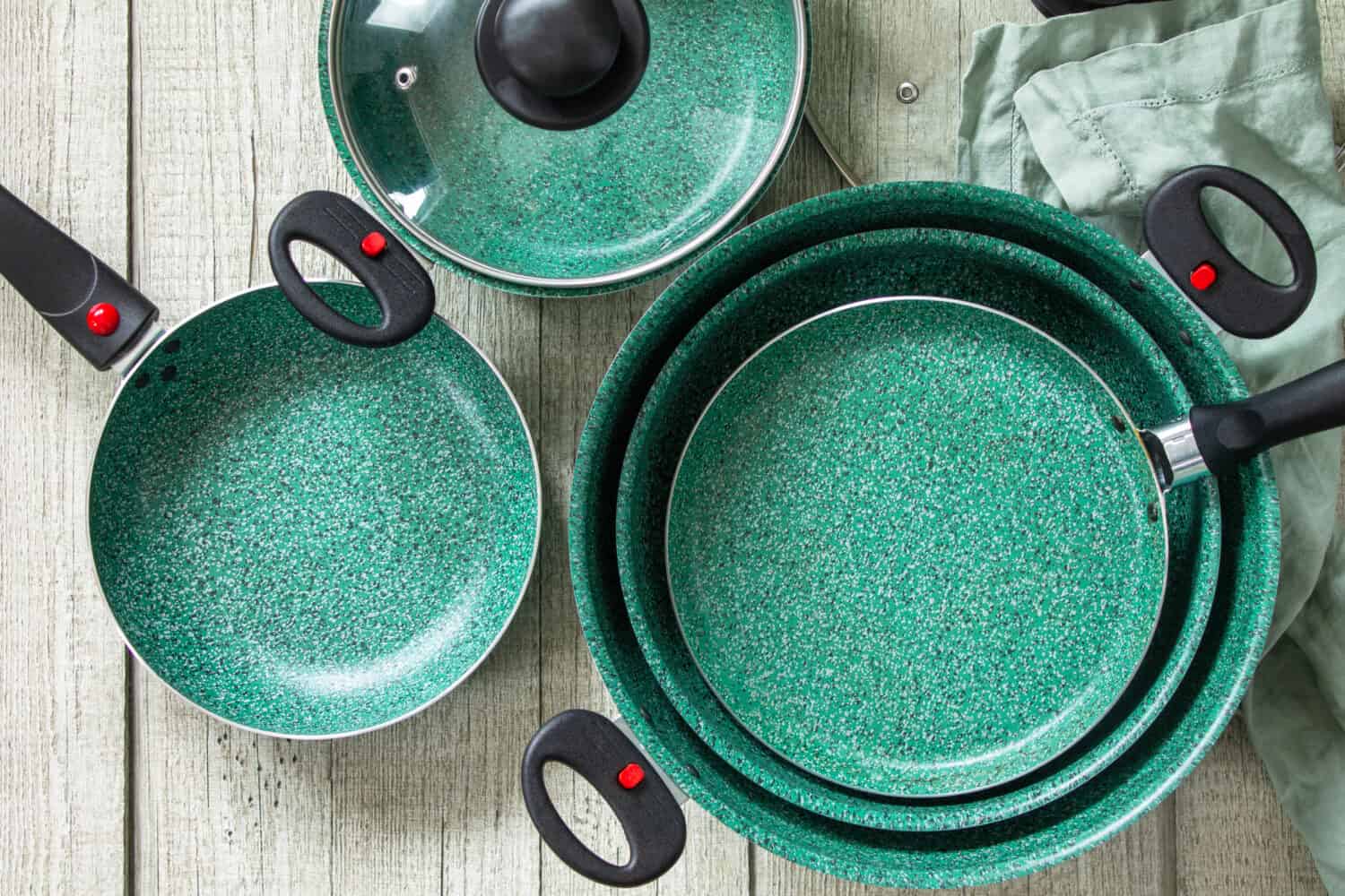 New set Empty fry pan green with ceramic coatingon on a rustic kitchen table. Top view flat lay background.