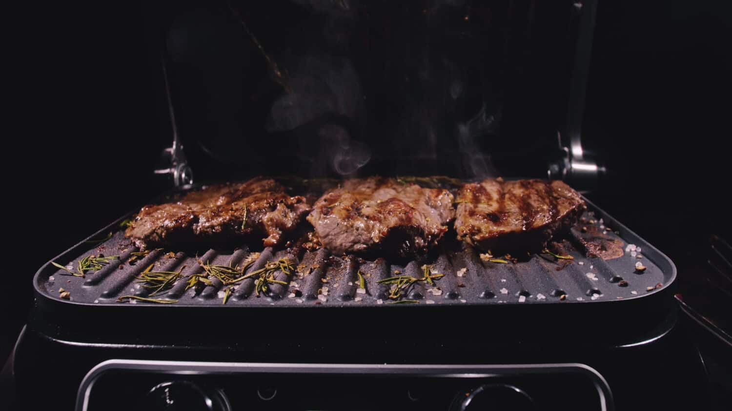 Delicious juicy meat steak cooking on grill. Prime beef fry on electric roaster, rosemary, black pepper, salt. Slow motion.