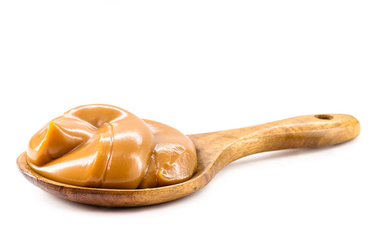 spoon with homemade dulce de leche, condensed cream or pasty caramel, isolated white background.