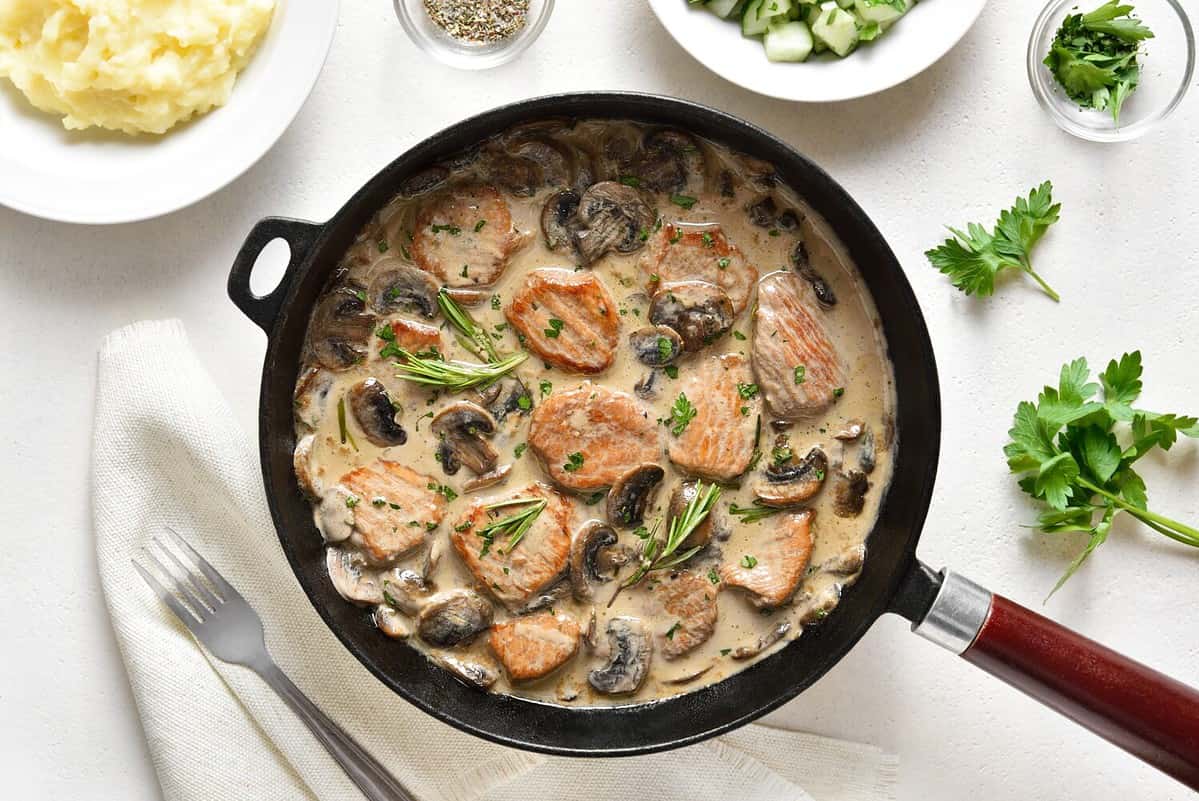 Pork medallions with mushroom sauce in cast iron pan over white stone background. Top view, flat lay