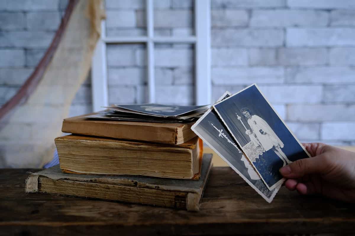 female hand holds vintage photos, retro photography of 1940-1950 on wooden table, old books, concept of genealogy, memory of ancestors, family tree, genealogy, childhood memories, family archive