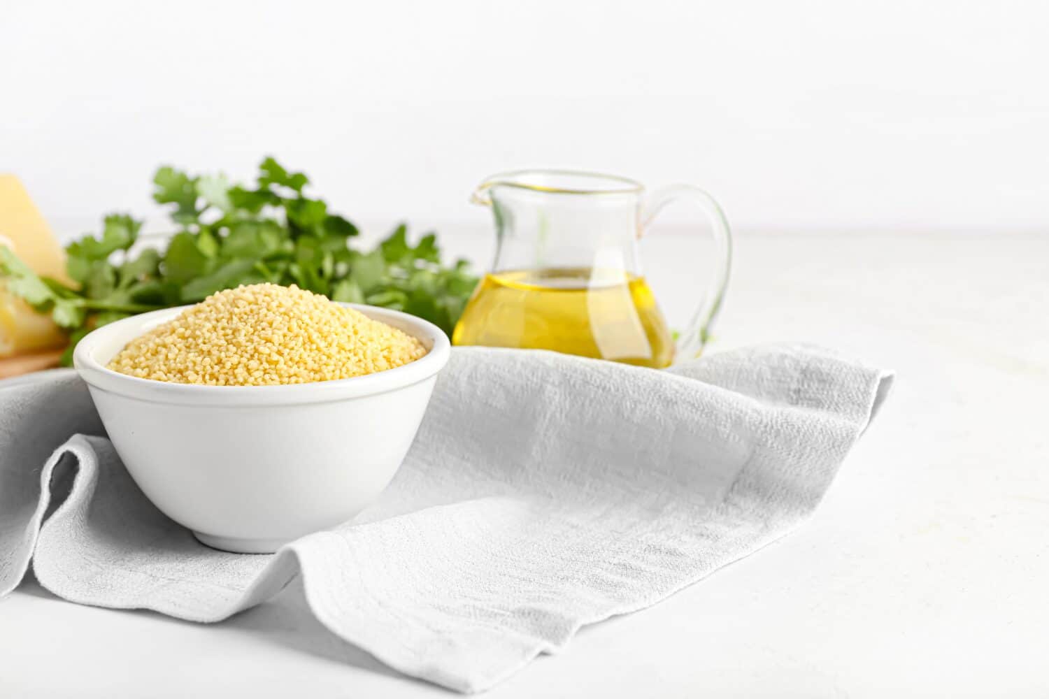 Bowl of raw couscous and oil on white background