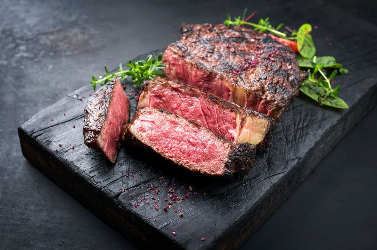 Barbecue dry aged wagyu entrecote beef steak roast with lettuce and salt as closeup on a charred wooden board