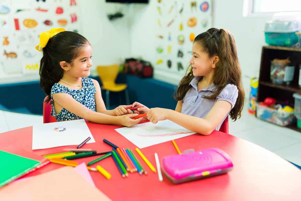 Adorable happy girls in preschool sharing their color pencils while coloring and learning in the classroom