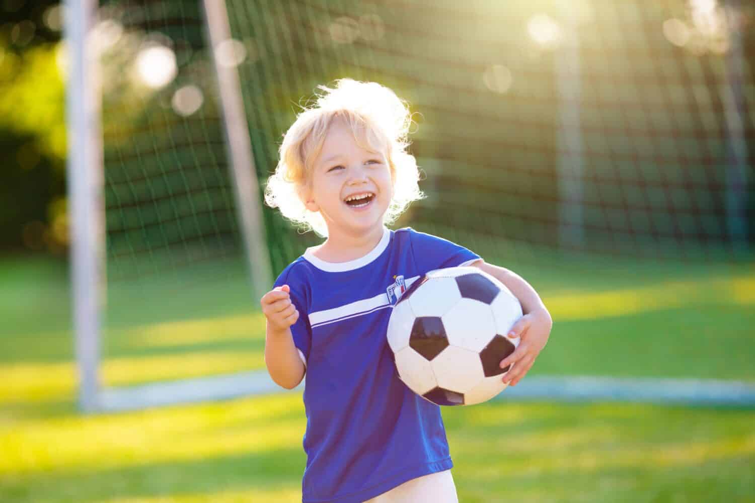 Kids play football on outdoor field. France team fans with national flag. Children score a goal at soccer game. Child in French jersey and cleats kicking ball. Fan celebrating victory at pitch.