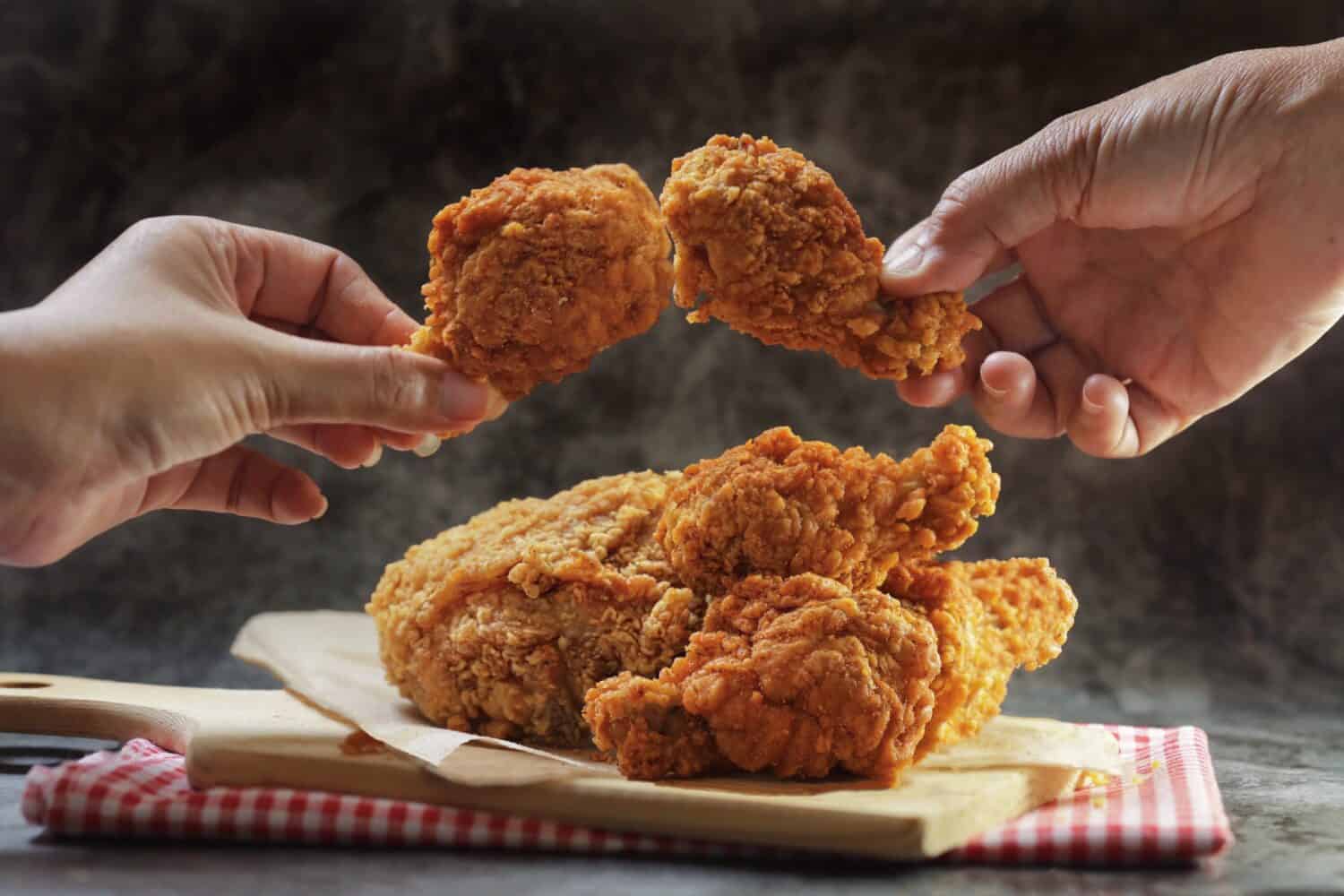 Woman hand taking the fried chicken wings by hands over dark background with copy space.