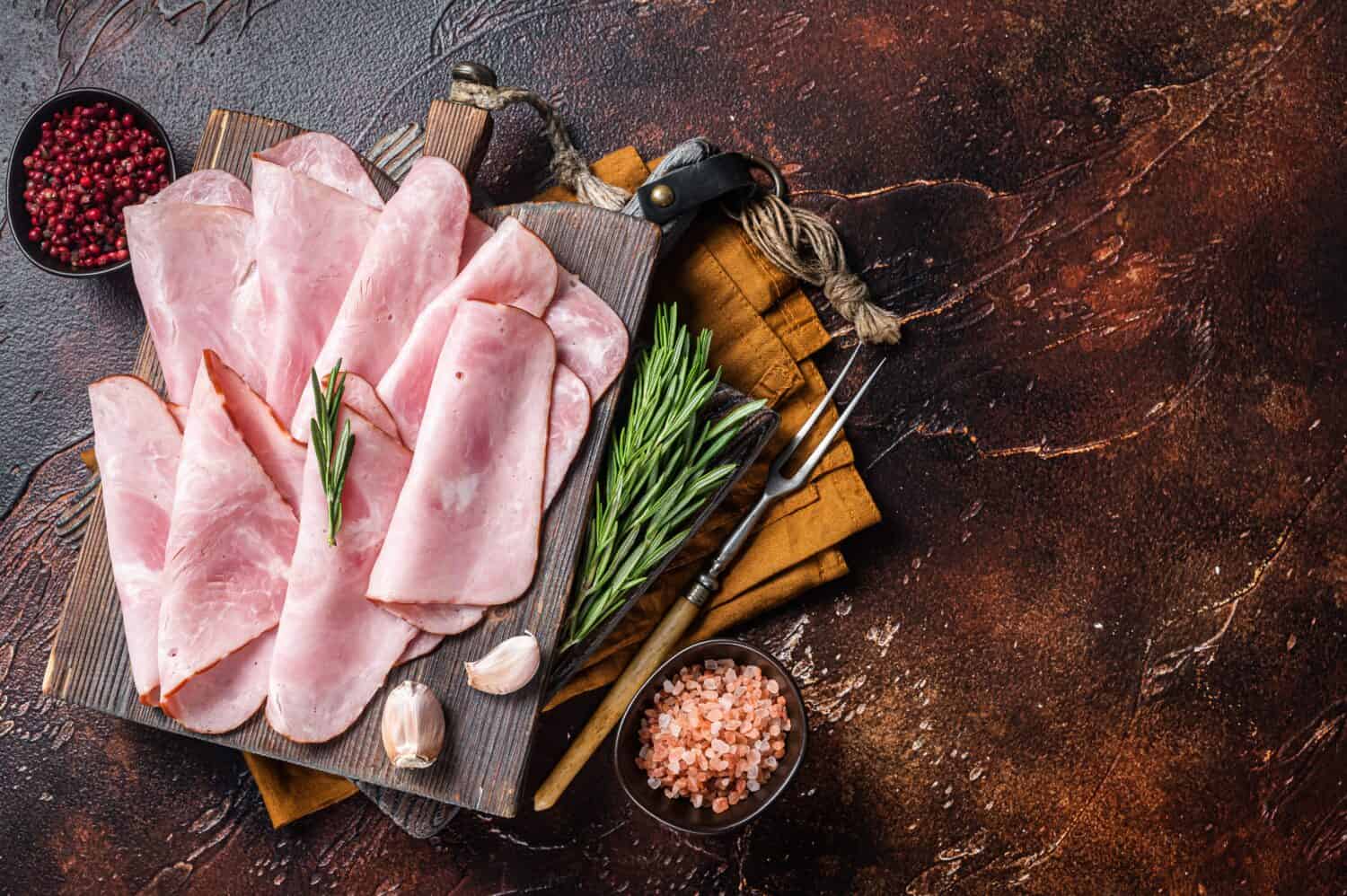 Flat slices of square sandwich ham with herbs. Dark background. Top view. Copy space.