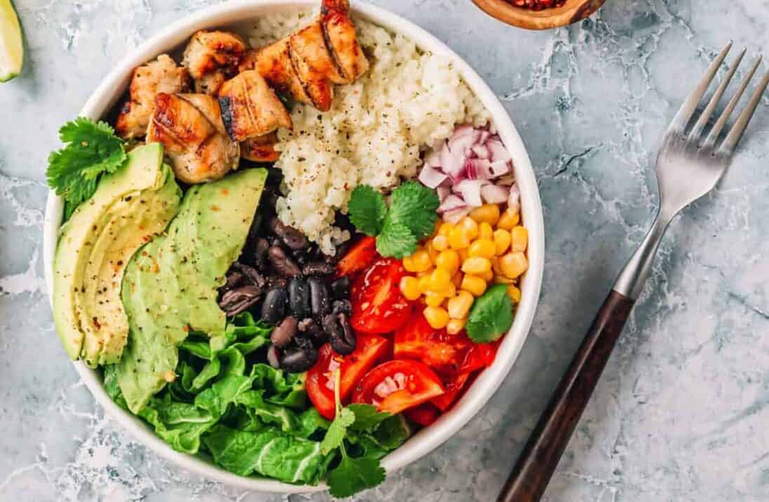 Mexican chicken burrito bowl with rice, beans, tomato, avocado,corn and lettuce.