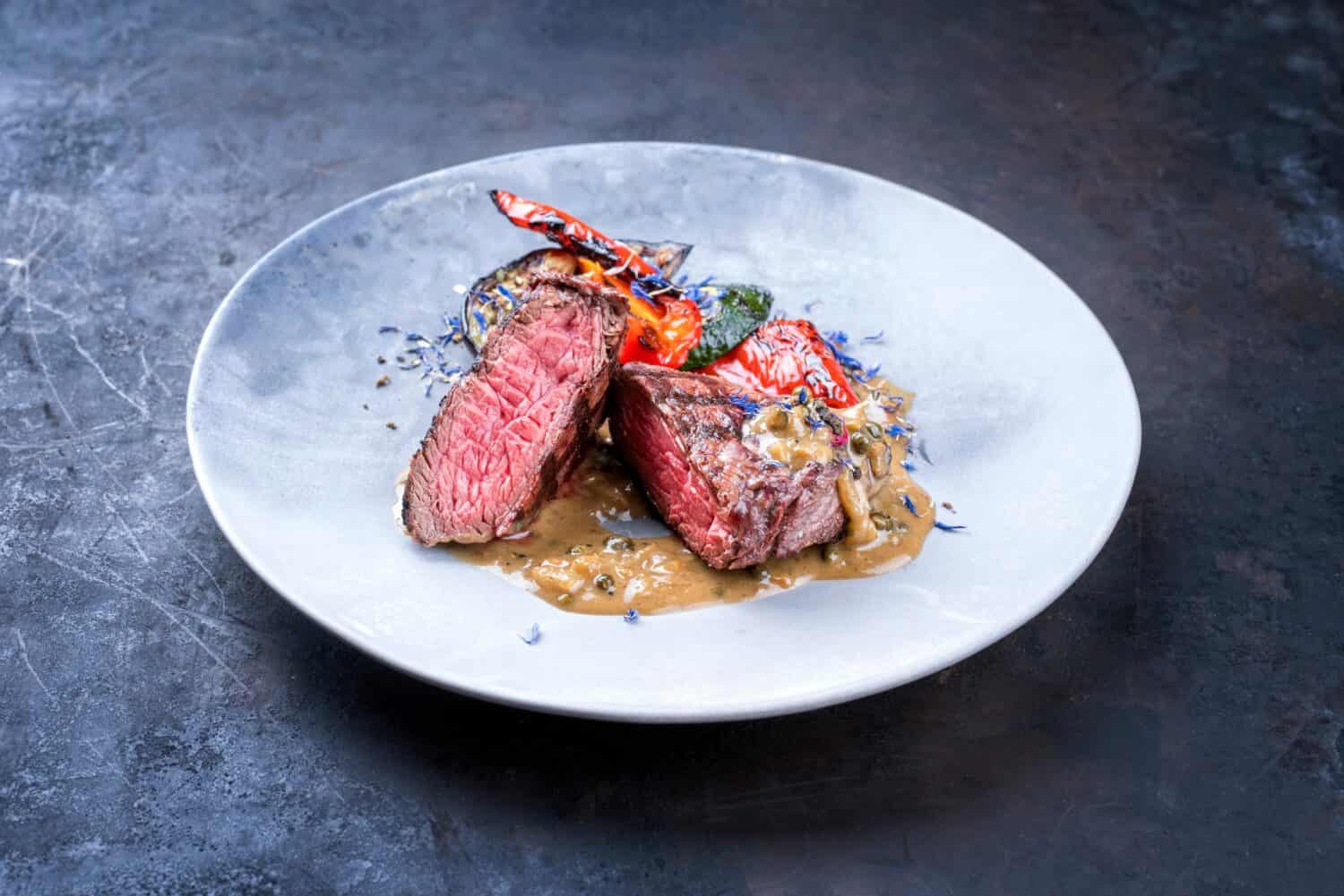 Modern style barbecue dry aged wagyu roast beef pepper steak with barbecue vegetable in pepper cream sauce served as close-up in a design plate 