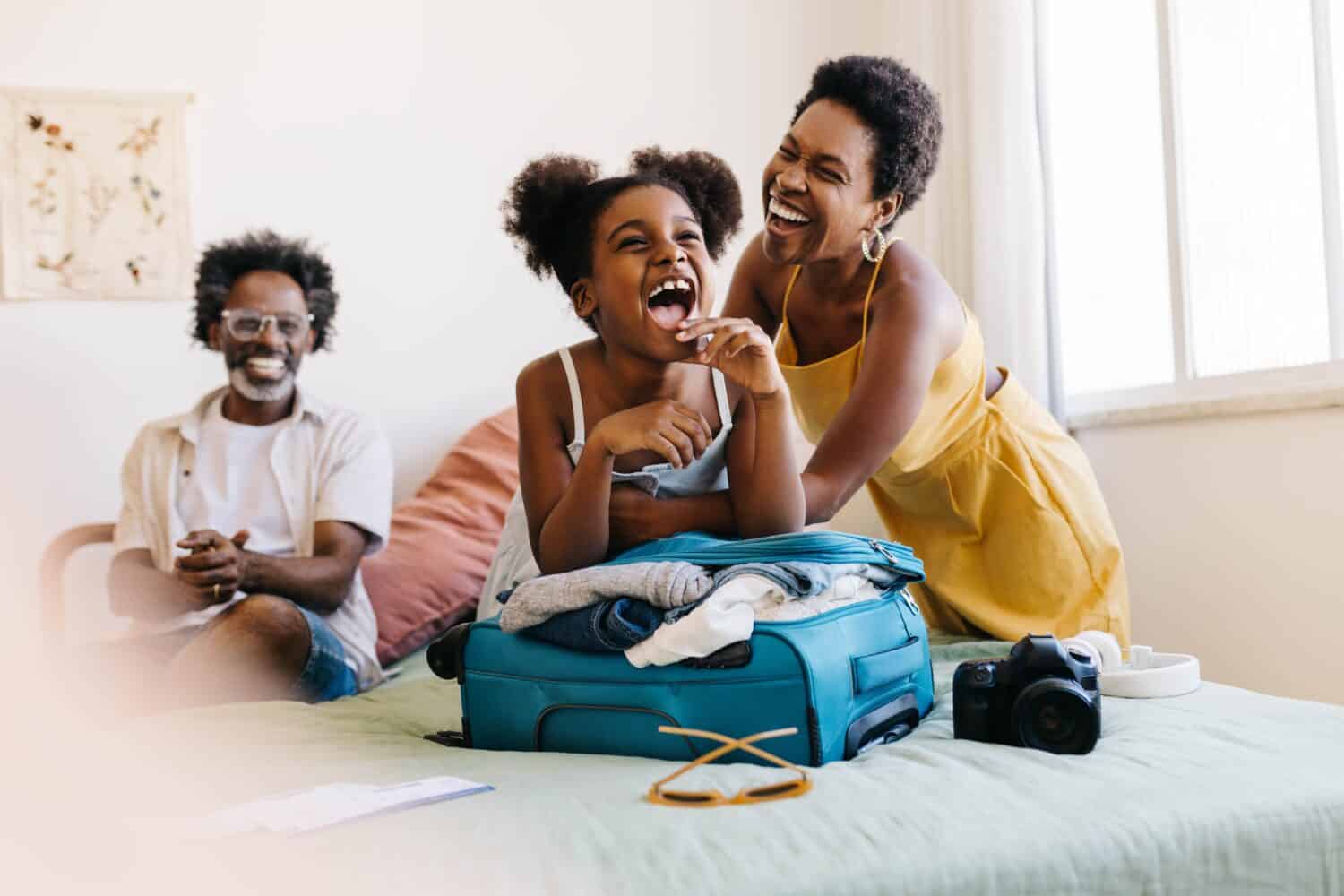 Happy family preparing for a vacation, laughing together as they pack travel essentials. Parents, along with their excited daughter, enjoy  planning and getting ready for a fun-filled holiday.