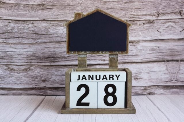 Chalkboard with January 28 calendar date on white cube block on wooden table.
