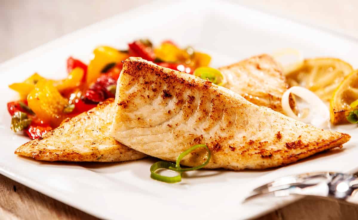 Two marinated grilled fresh tilapia fillets served with colorful roasted vegetables as a delicious seafood appetizer to dinner