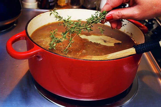 Woman placing sprig of thyme in a pot of French onion soup