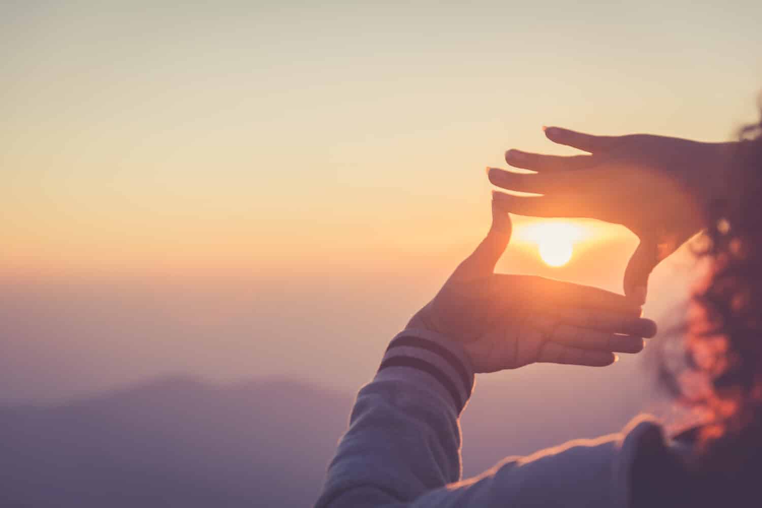 The woman making frame round the sun with her hands in sunrise,copy space,warm retro tone.