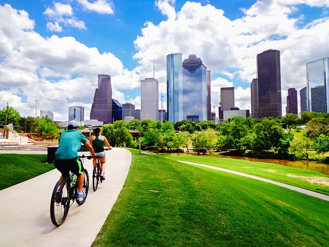 Riding Bikes on Paved Trail in Houston Park (view of river and skyline of downtown Houston) - Houston, Texas, USA