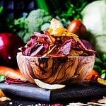 Vegan snacks, multicolored vegetable chips in wooden bowl, background from set of fresh farmer vegetables, still life, selective focus