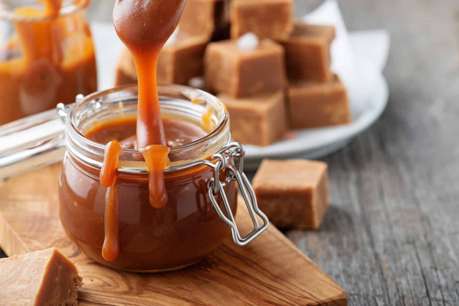 Homemade salted caramel sauce in jar on rustic wooden table.