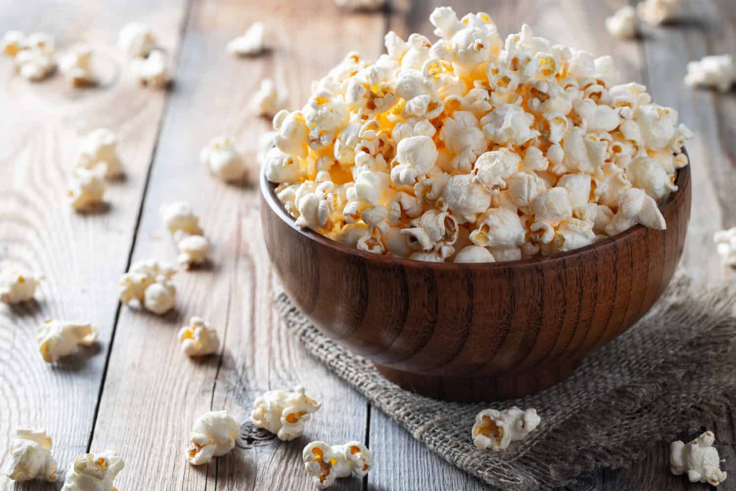 A wooden bowl of salted popcorn at the old wooden table. Dark background. selective focus