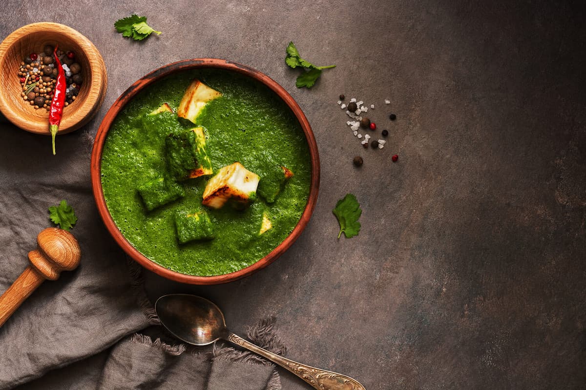 Palak paneer or Spinach and Cottage cheese curry,mortar with spices on a dark background. Traditional Indian dish. Top view, copy space