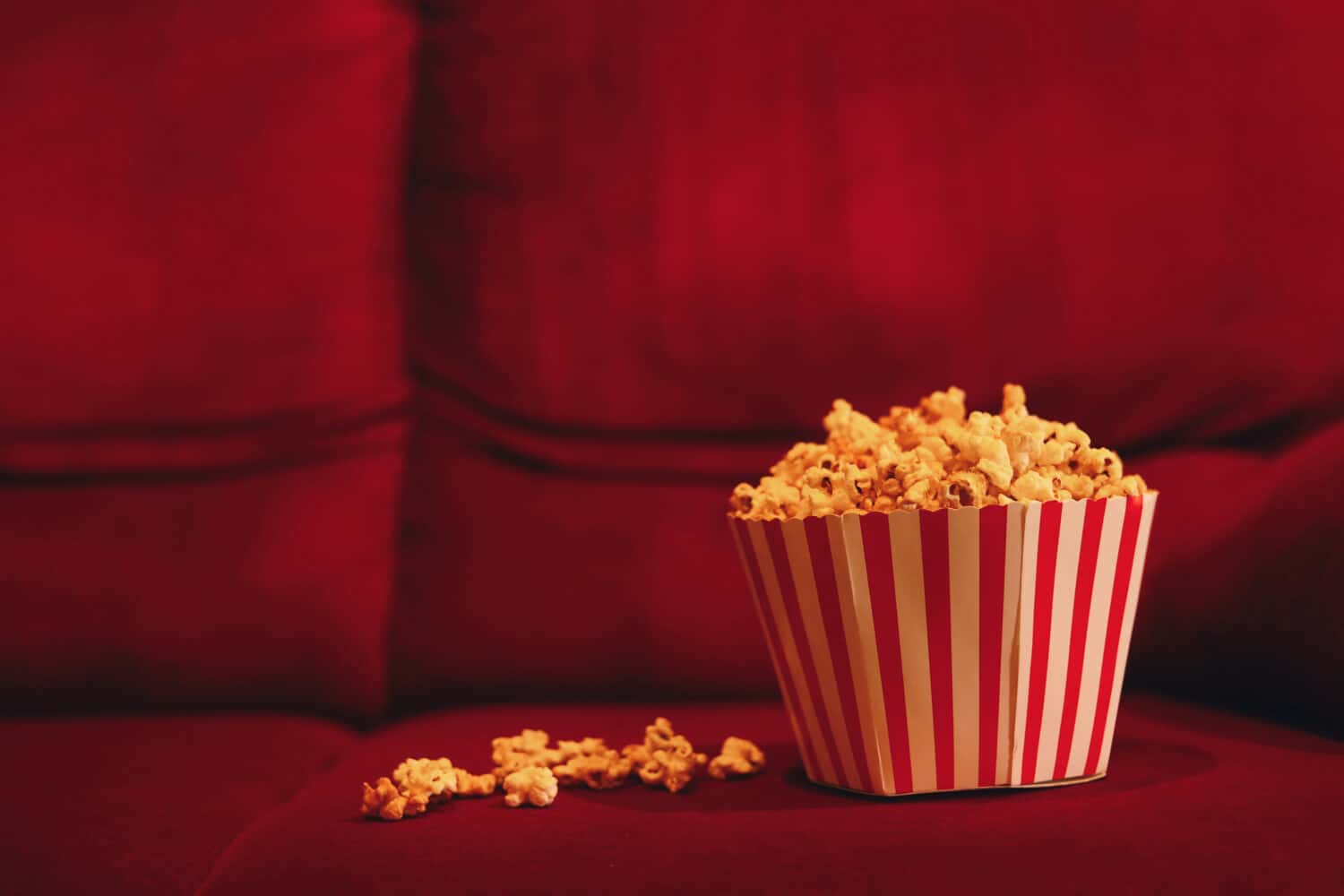 Popcorn bucket on red sofa at cinema.