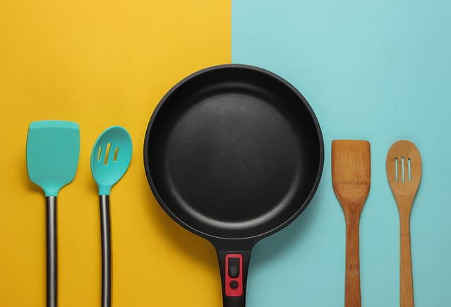 Non-stick pan with cooking spatula on blue yellow background. Cooking minimalism concept. Studio shot. Top view