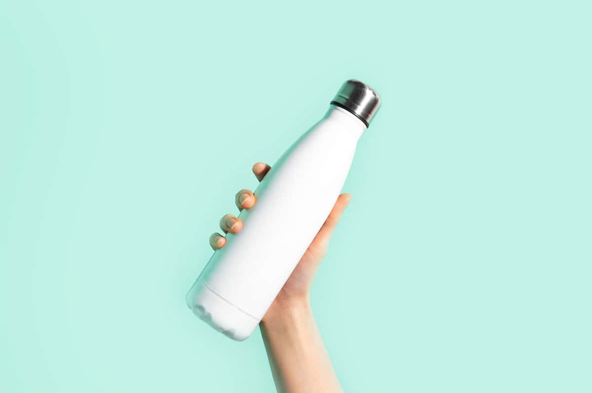 Close-up of female hand, holding white reusable steel stainless eco thermo water bottle with mockup, isolated on background of cyan, aqua menthe color. Be plastic free. Zero waste.