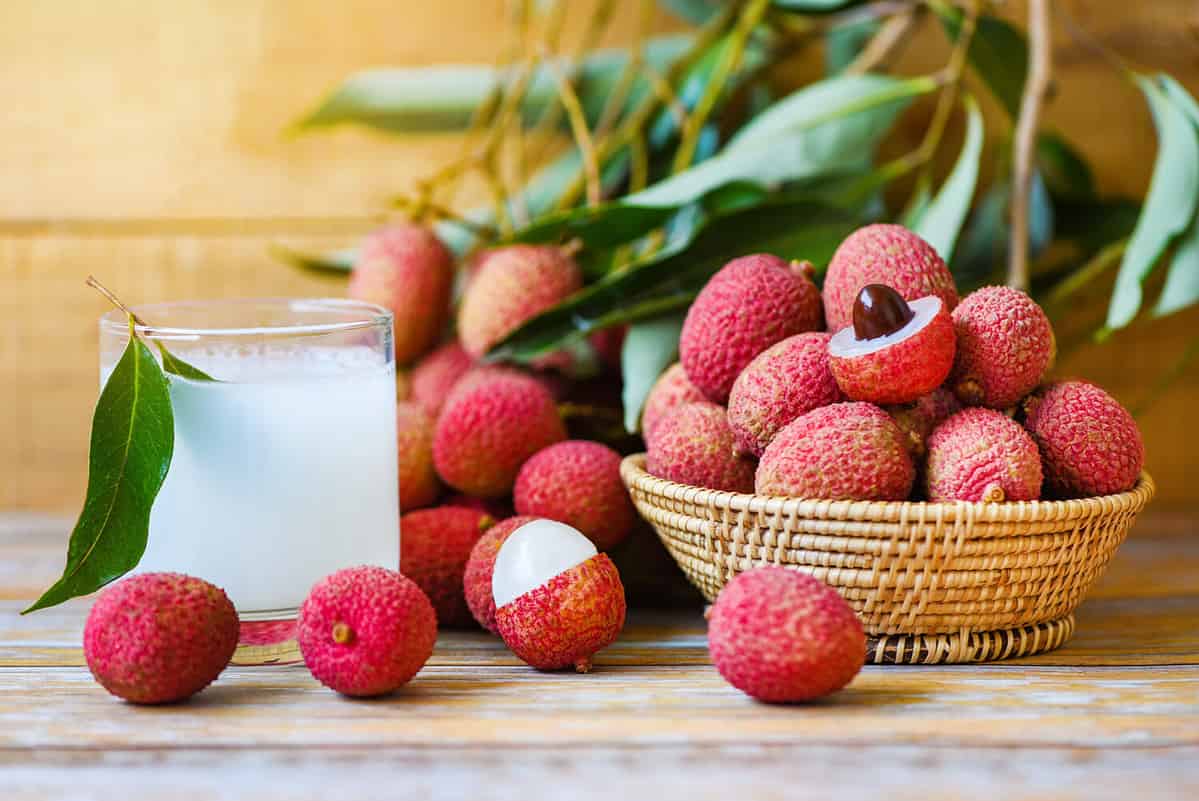 Lychee juice on wooden table / Fresh lychee drink and slice peeled with green leaves harvest in basket from tree tropical fruit summer in Thailand