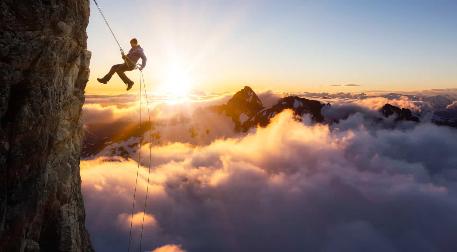 Epic Adventurous Extreme Sport Composite of Rock Climbing Man Rappelling from a Cliff. Mountain Landscape Background from British Columbia, Canada. Concept: Explore, Hike, Adventure, Lifestyle