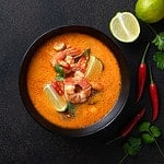tom yum kung Spicy Thai soup with shrimp in a black bowl on a dark stone background, top view, copy space