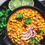 Vegan chickpea curry with rice and cilantro in a black bowl, dark background. Indian cuisine concept.