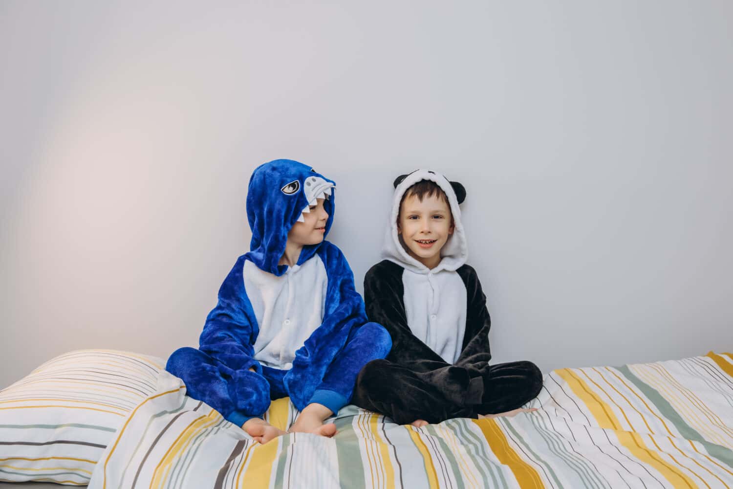 Two brothers 5-7 years old are playing at home in the children's room on the bed in funny pajamas. 