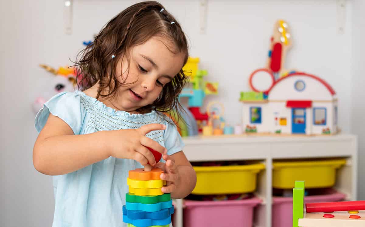 Two-year-old girl, of Caucasian origin, playing and learning very concentrated and smiling with some educational wooden toys in the kindergarten.