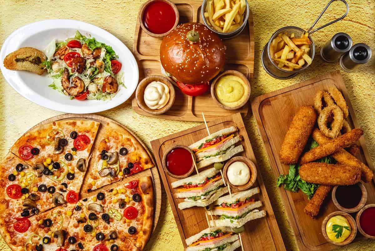 fast food mix mozzarella sticks club sandwich hamburger mushroom pizza caesar shrimp salad french fries ketchup mayo and cheese sauces on the table