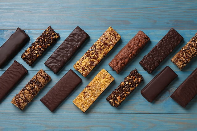 Different tasty protein bars on light blue wooden table, flat lay