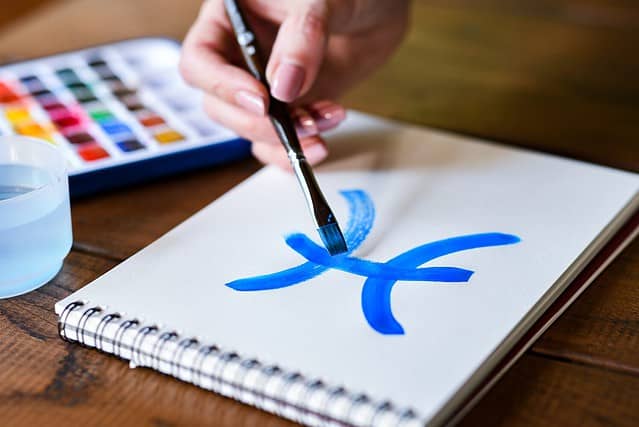 Women's hands paint with blue paint and brush the sign of the zodiac pisces horoscope astrology